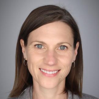 Dr. Amanda Spivak smiles at the camera with burgundy hair and a grey sweater.