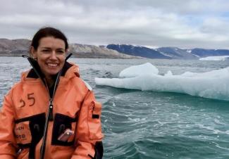 Dr. Karen Lloyd stands in front of a glacier in an orange winter coat