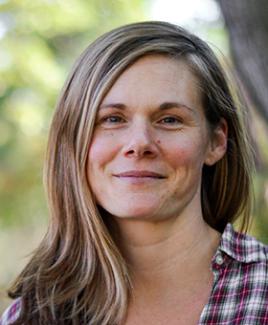 Dr. Katie Hill smiles in the camera with long sandy brown hair and a red plaid button up.