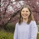 Dr. Erin Dolan smiles widely into the camera. She is wearing a soft lilac sweater and he face is framed by mousy brown shoulder length hair.