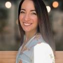 Dr. Valerie De Anda stands sideways with her head turned towards the camera smiling. Her dark brown hair falls behind her back against her white button up. 