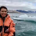 Dr. Karen Lloyd stands in front of a glacier in an orange winter coat