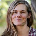 Dr. Katie Hill smiles in the camera with long sandy brown hair and a red plaid button up.